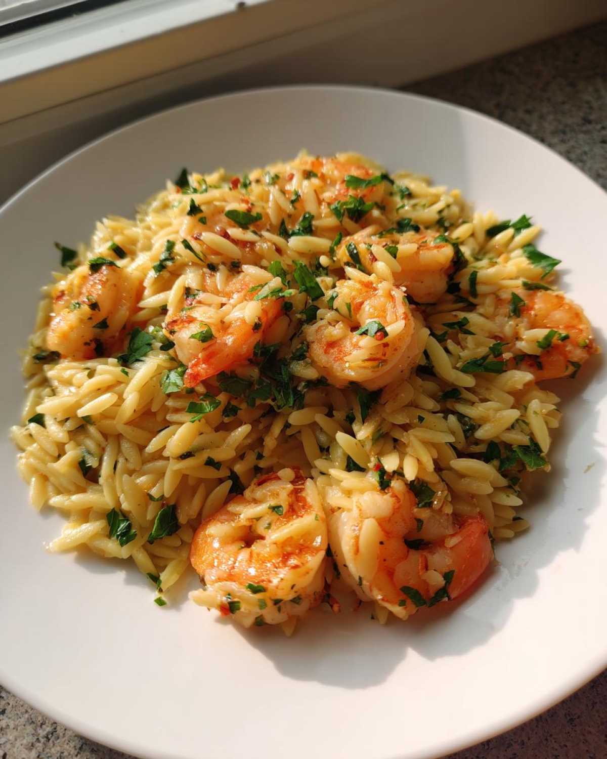 A white plate filled with Lemon Orzo Shrimp, garnished generously with fresh chopped parsley.