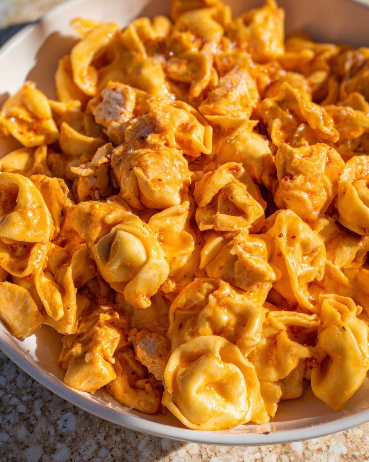Close-up of rich, creamy Marry Me Chicken Tortellini coated in an orange-hued sauce, served in a white bowl.