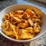 Close-up of a white bowl filled with creamy Marry Me Chicken Tortellini, topped with herbs.