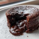 A close-up of a freshly baked Molten Chocolate Lava Cake with the center oozing rich chocolate sauce, dusted with powdered sugar.