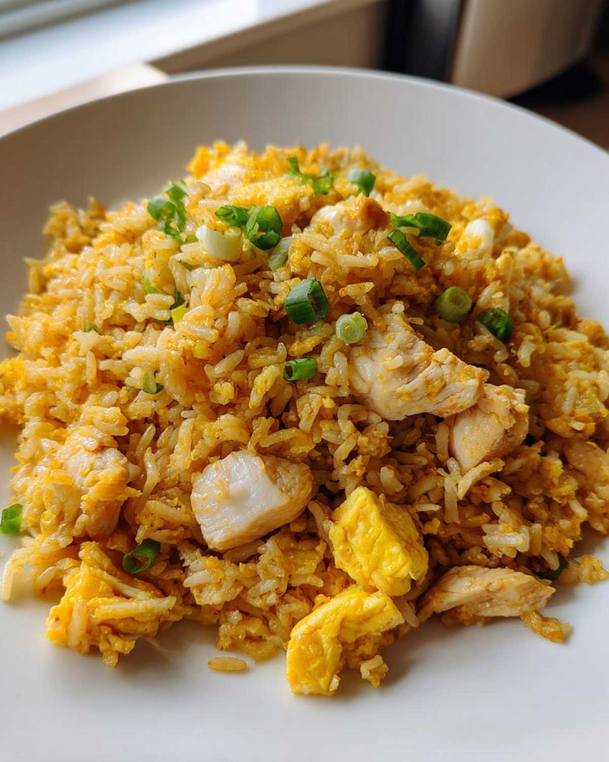 A close-up of a serving of golden Pineapple Fried Rice with Chicken chunks and scrambled egg, garnished with green onions.