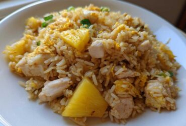 A serving of vibrant Pineapple Fried Rice with Chicken, featuring chunks of pineapple, white meat chicken, and scrambled egg.