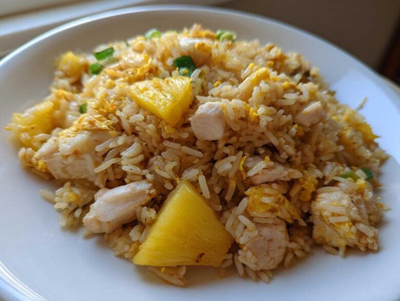 A serving of vibrant Pineapple Fried Rice with Chicken, featuring chunks of pineapple, white meat chicken, and scrambled egg.