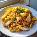 A close-up of vibrant Pineapple Fried Rice with Chicken, featuring yellow rice, chunks of white chicken, and pineapple pieces, garnished with green onions.