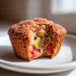 Close-up of a Rhubarb Muffins with Cinnamon Sugar Topping with a bite taken out, showing chunks of pink and green rhubarb inside.