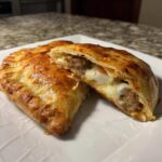A golden-brown Sausage and Pepper Calzone cut in half showing melted cheese and sausage filling.