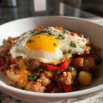 A close-up of a Sausage and Potato Breakfast Bowls topped with a perfectly fried egg and fresh herbs.