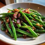 Close-up of bright green Sautéed Green Beans with Crispy Bacon and caramelized onions served in a white bowl.