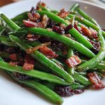 Close-up of bright green Sautéed Green Beans with Crispy Bacon bits served on a white plate.