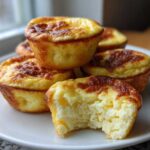 A stack of golden-brown Starbucks Copycat Egg Bites on a white plate, with one bite taken out showing the fluffy interior.