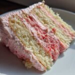 Close-up of a moist slice of Strawberry Vanilla Cake with Frosting, showing layers of vanilla cake and pink strawberry filling.