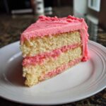 A close-up of a slice of Strawberry Vanilla Cake with Strawberry Frosting showing three layers.