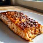Close-up of a perfectly cooked Texas Roadhouse Style Baked Salmon fillet with a dark, glossy, whole-grain mustard glaze.